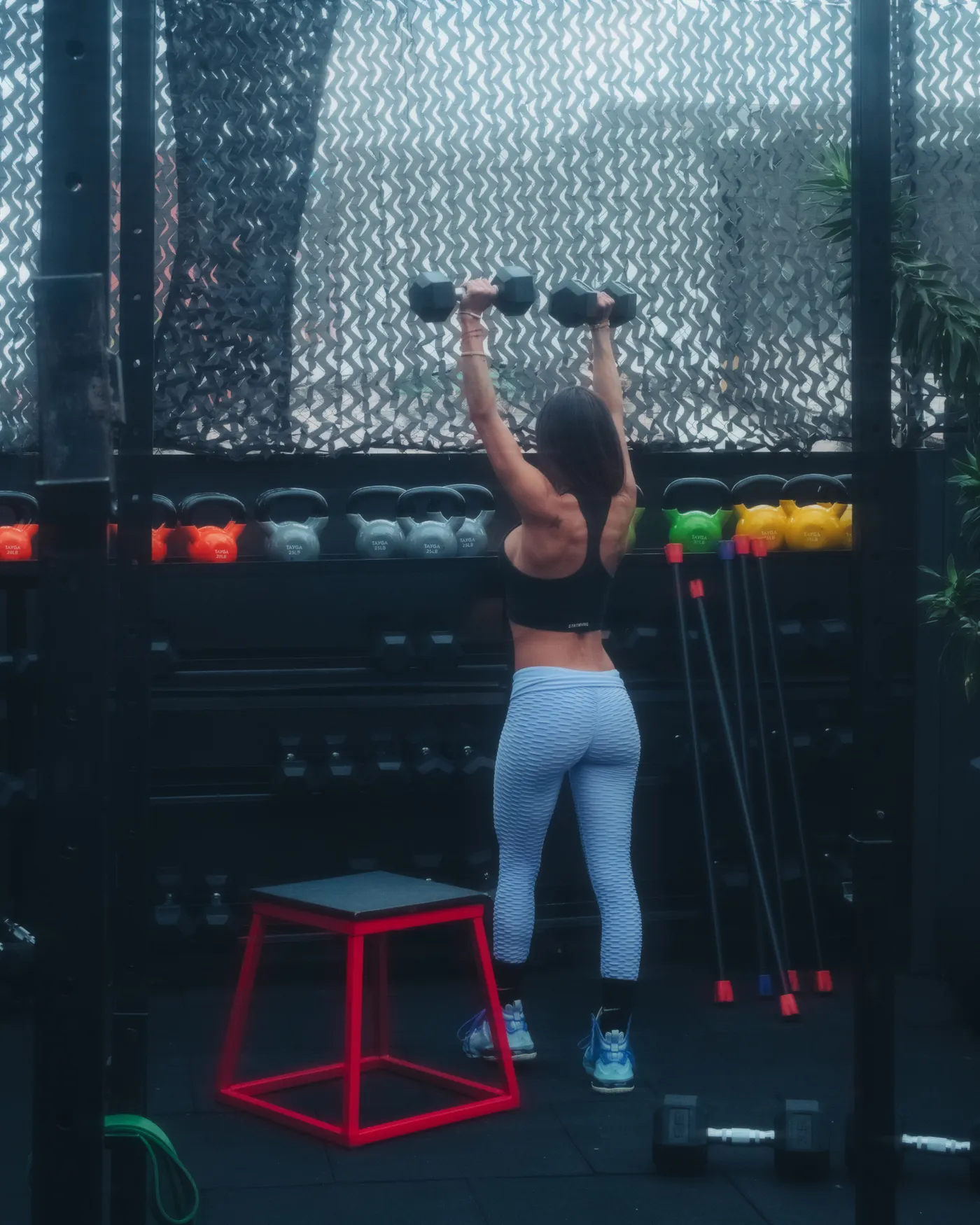 Woman pressing dumbbells overhead during a strength session