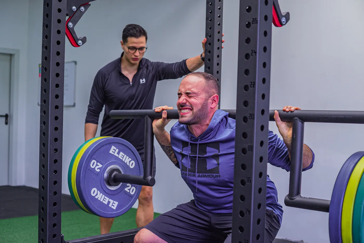 Athlete squatting with a loaded barbell under a coach's supervision