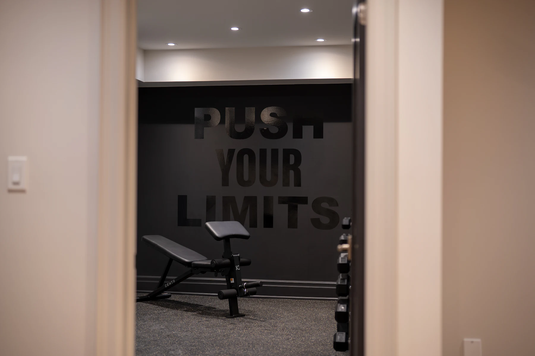 Dark home gym with dumbbells and a motivational wall