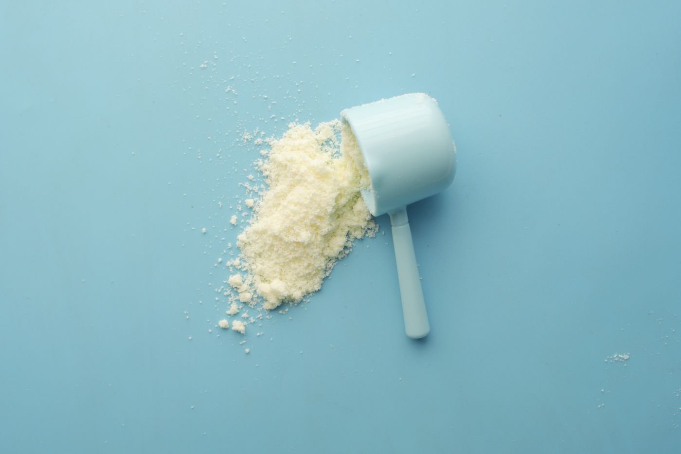 White powder in a measuring scoop on a blue background, illustrating supplement dosing