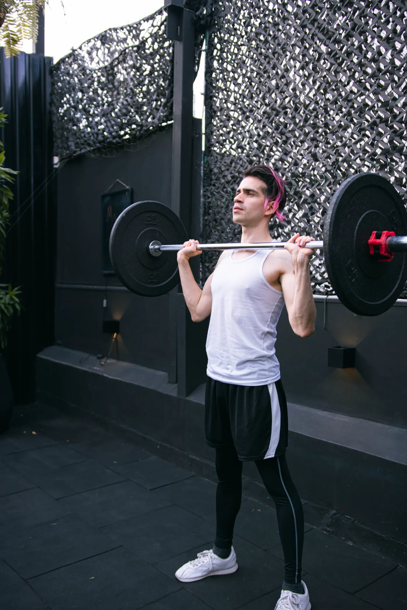 Man performing a standing barbell shoulder press outdoors