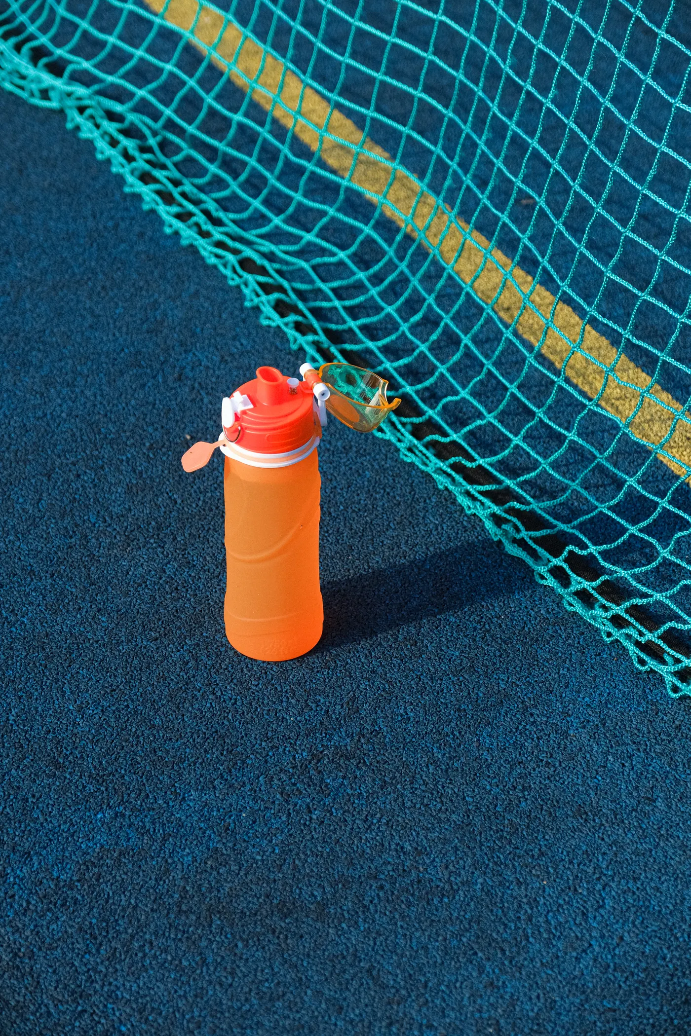 Orange water bottle resting on a blue sports court