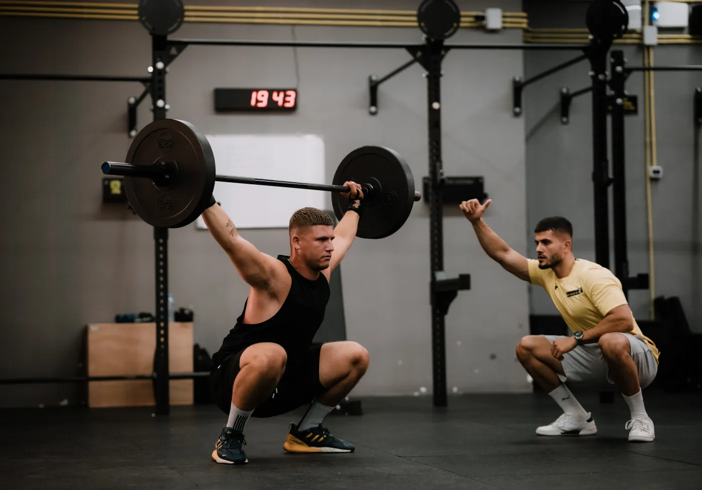 Barbell athlete lifting overhead with coach nearby