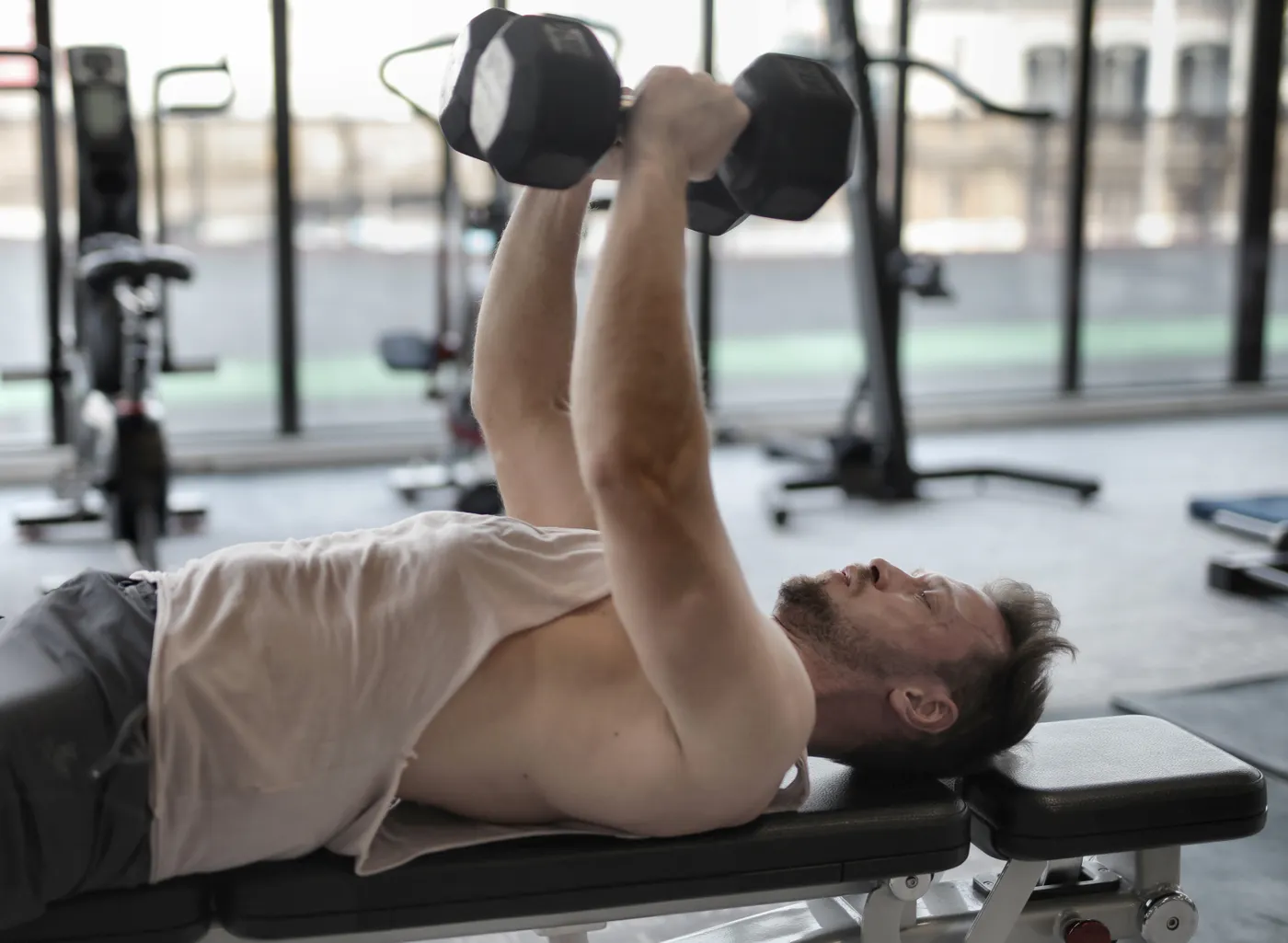 Man performing a supported dumbbell press on a gym bench