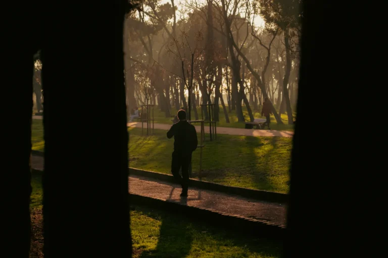 Man walking along a sunlit park path at sunset, illustrating evening exercise