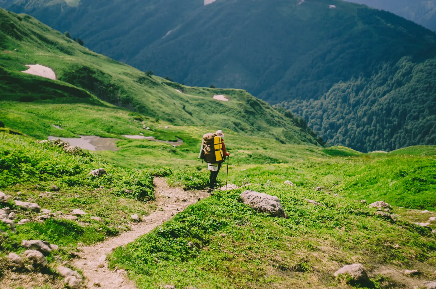 Hiker carrying a large backpack along a green mountain trail