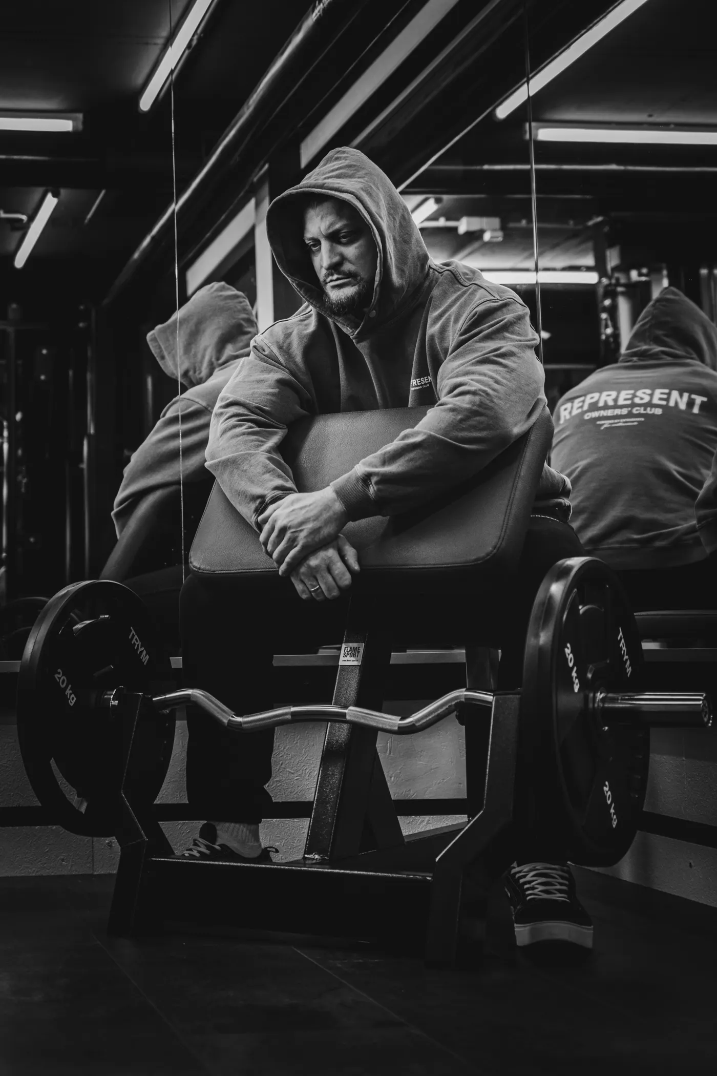 Athlete in a hoodie resting beside gym weights