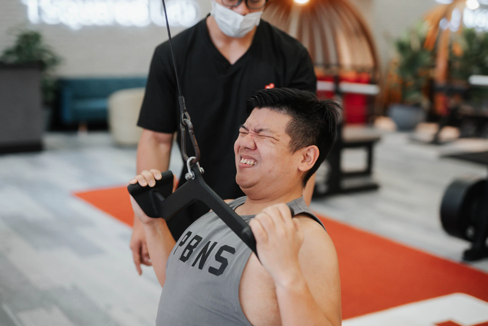 Athlete performing a cable pulling exercise with a trainer nearby