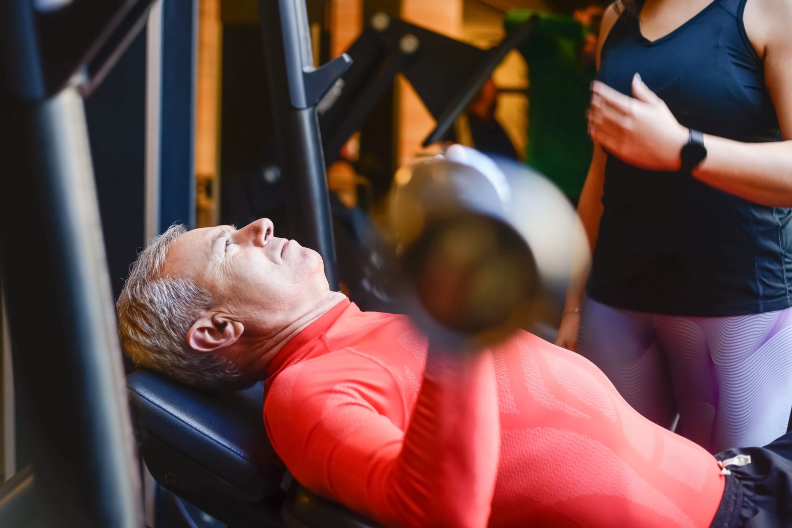 Older man performing supervised barbell exercise at a gym