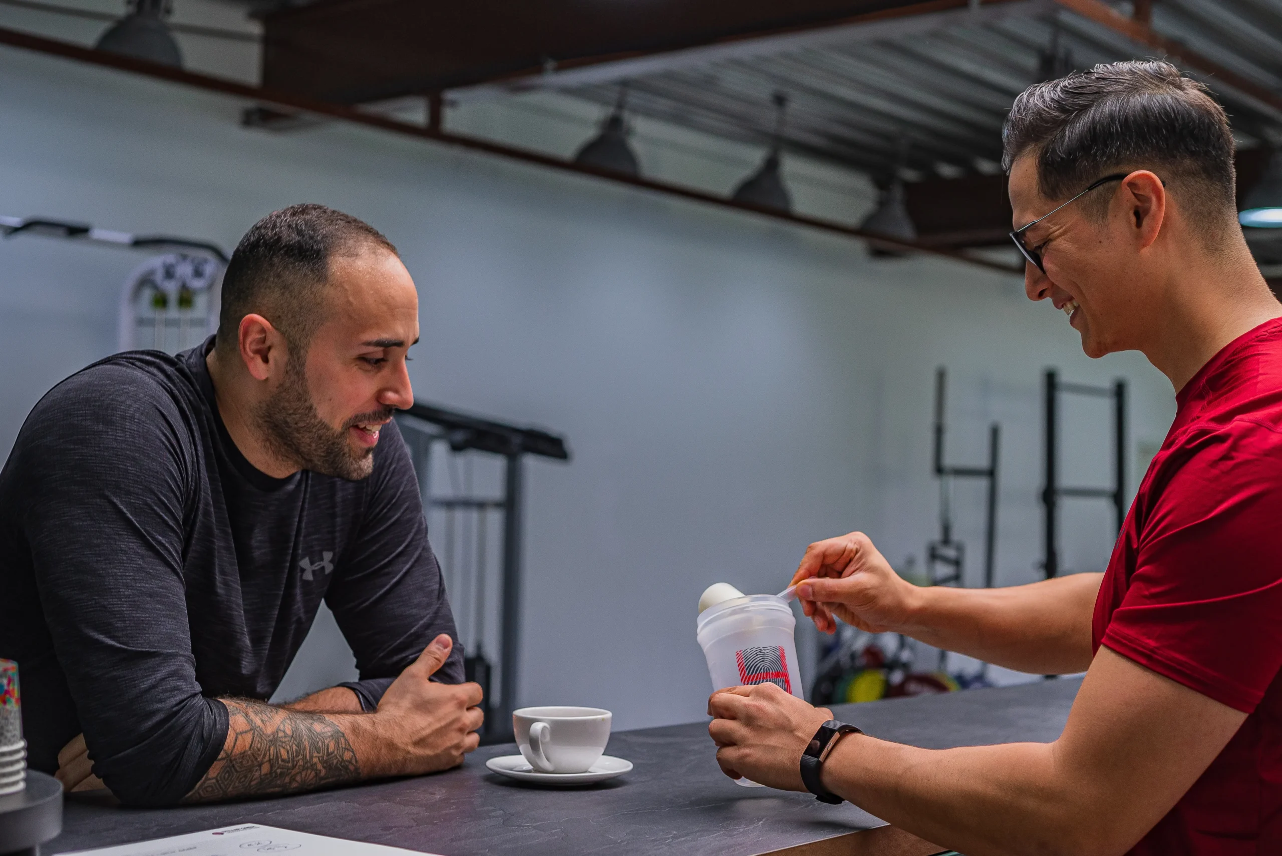 Two athletes preparing a protein drink together at a gym counter