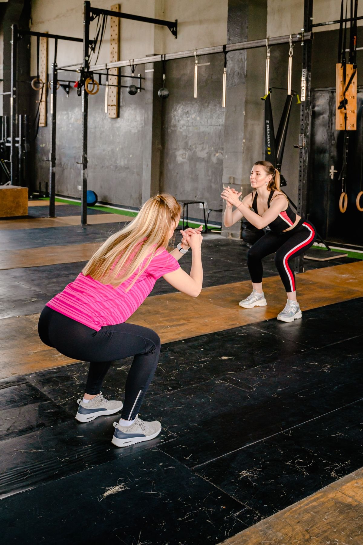 Two women performing bodyweight squats in a gym