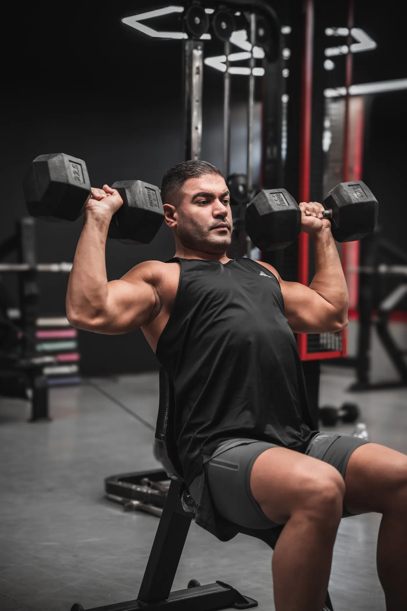 Man performing a dumbbell shoulder press in a modern gym