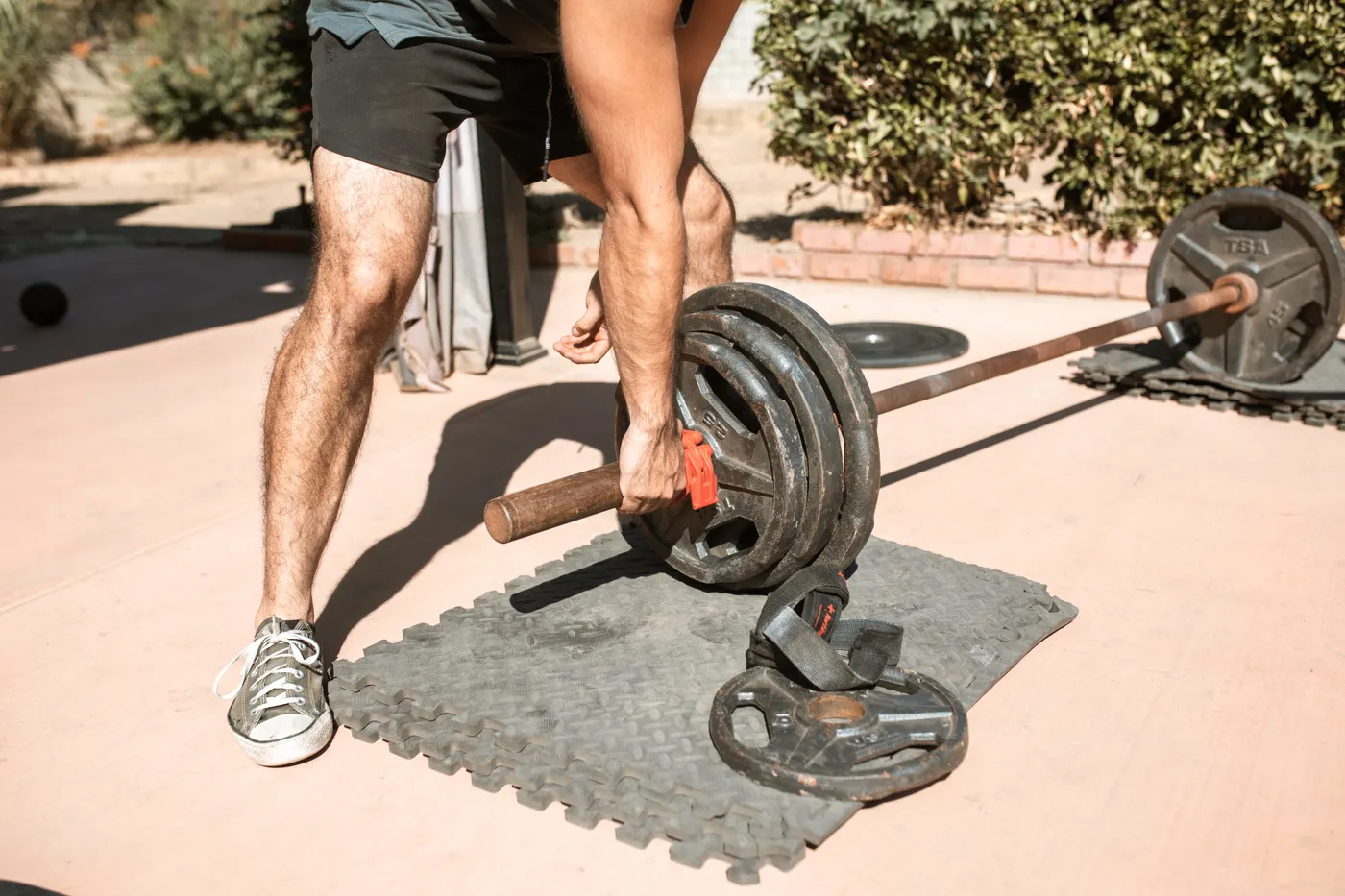 Man performing outdoor barbell strength work with lower-leg muscles visible