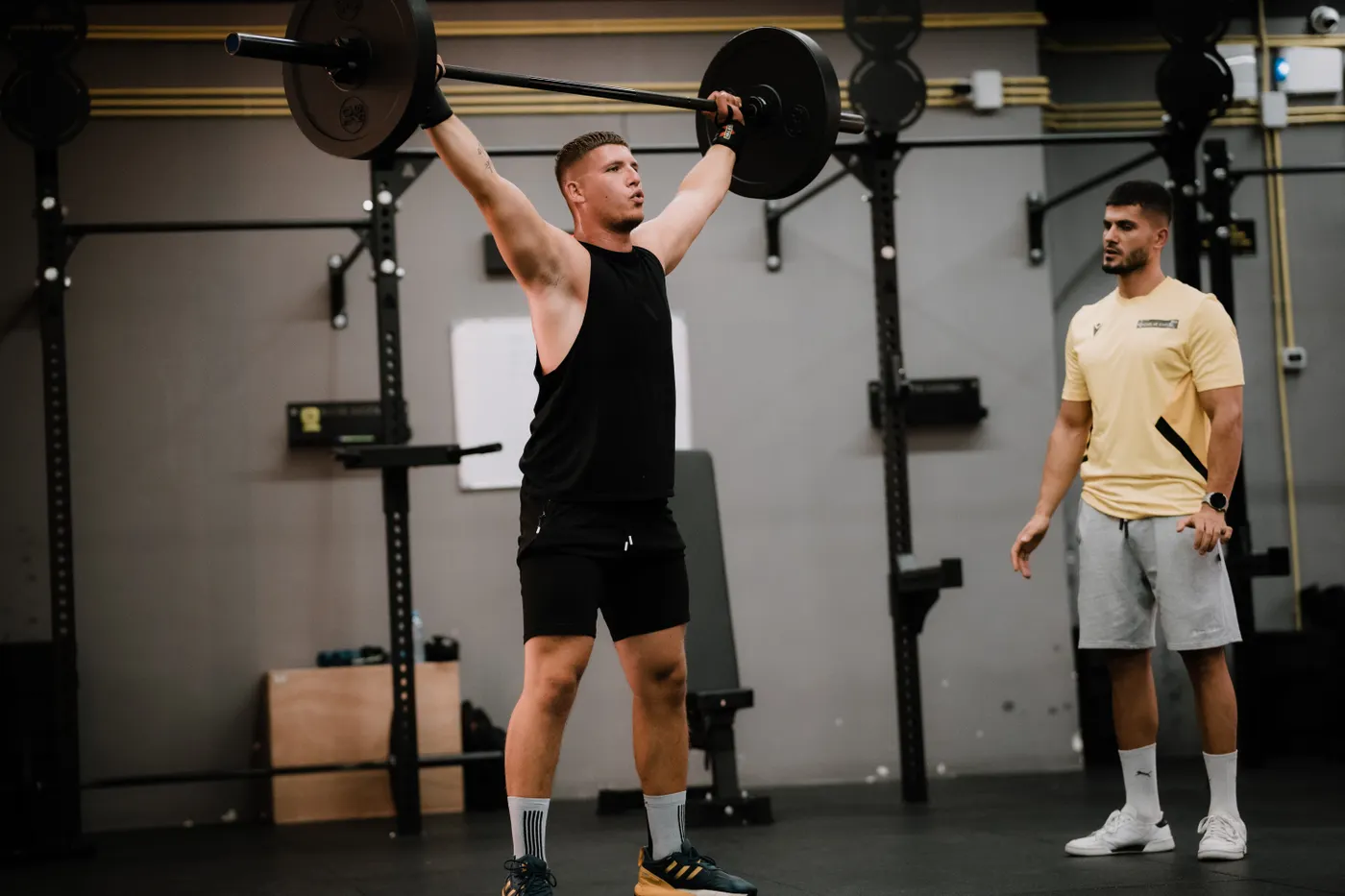 Athlete performing a heavy barbell lift in a gym with a trainer