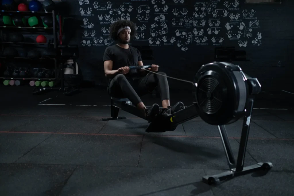 Man rowing hard on an indoor ergometer in a dark gym