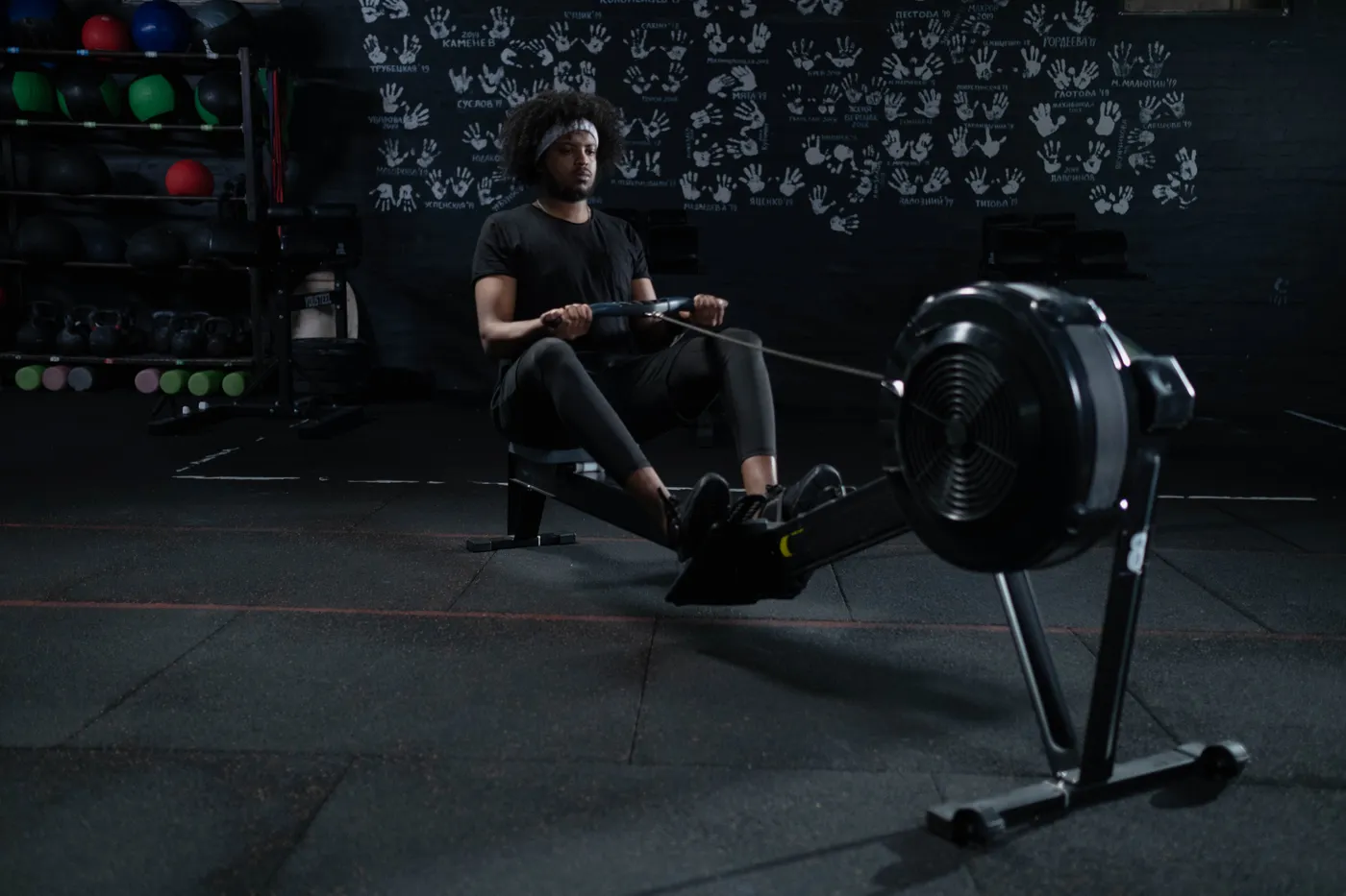 Man rowing hard on an indoor ergometer in a dark gym