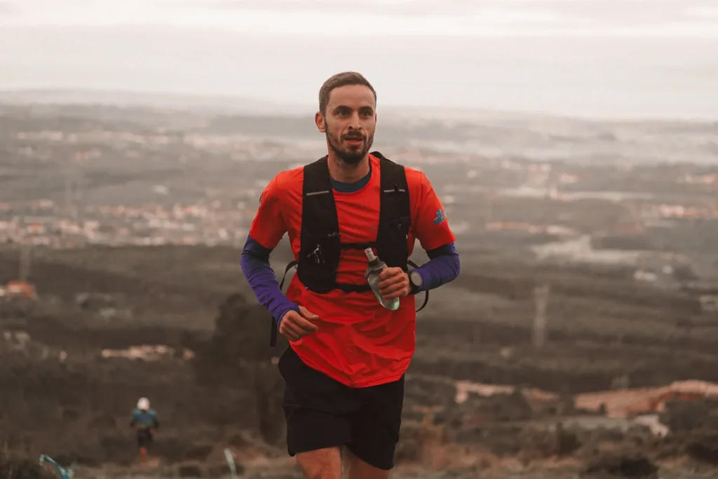 Runner in an orange shirt climbing a rugged mountain trail