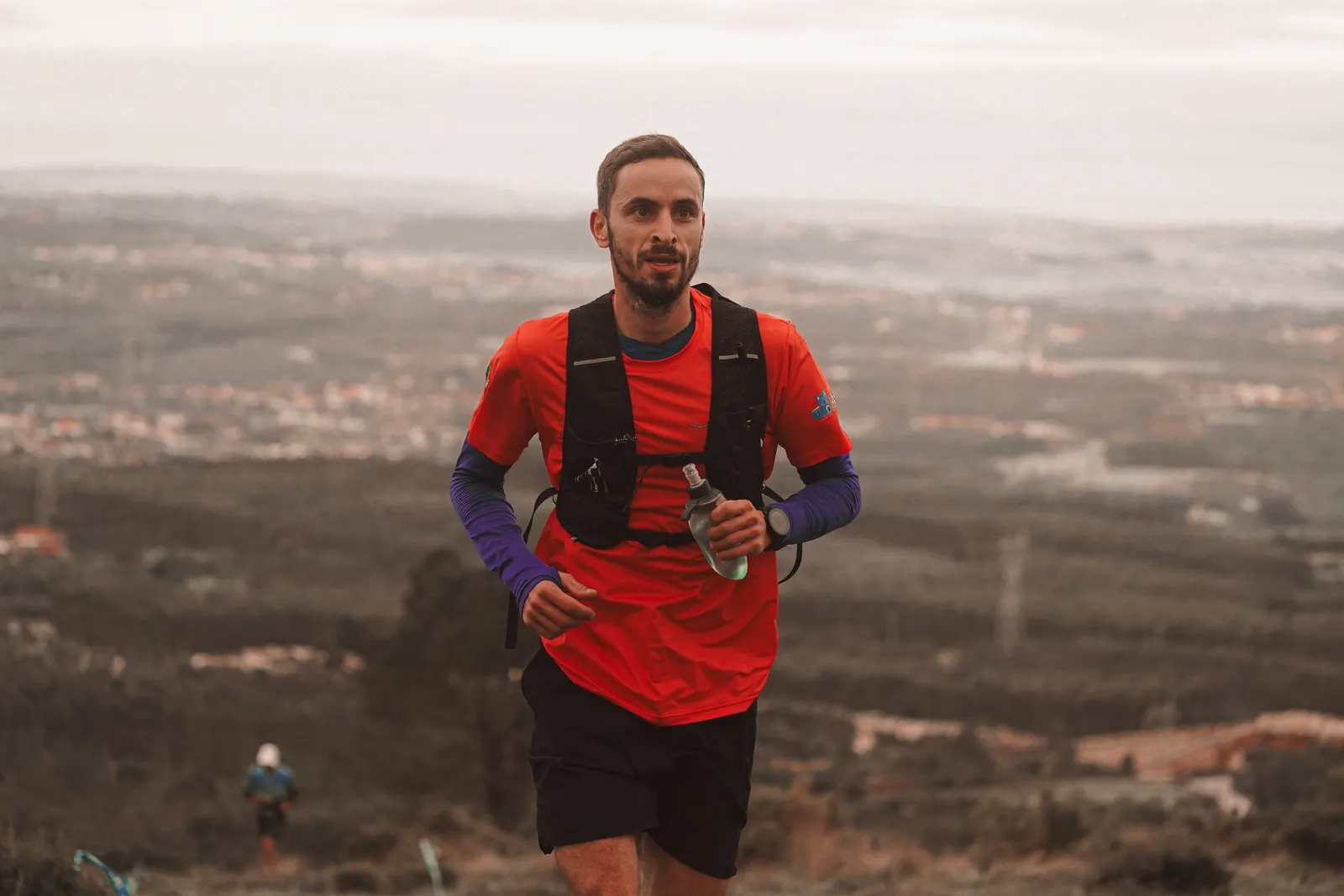 Runner in an orange shirt climbing a rugged mountain trail