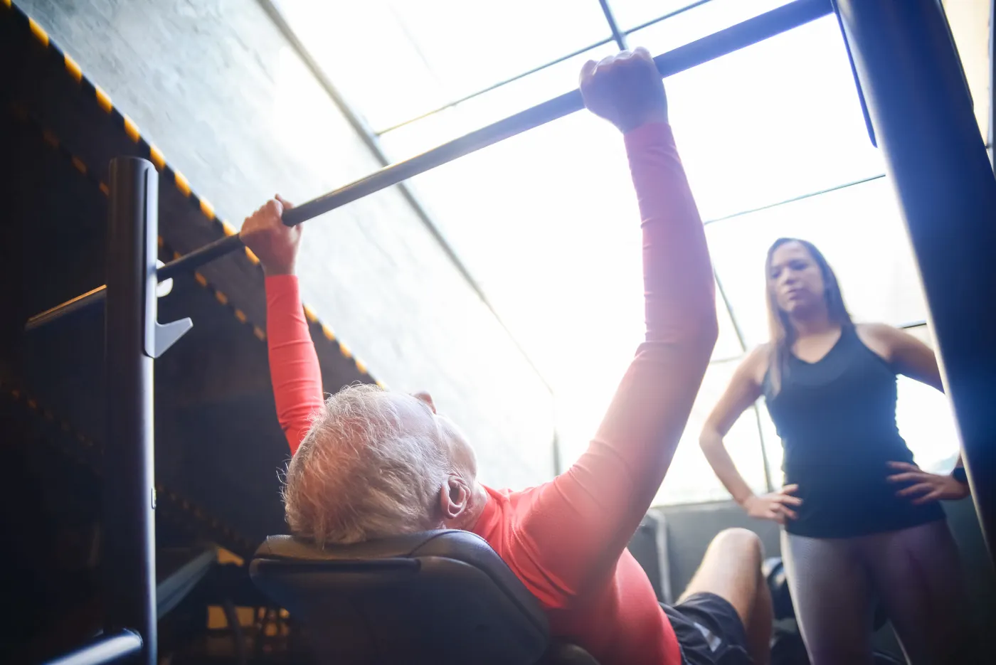 Older man bench pressing with a trainer nearby