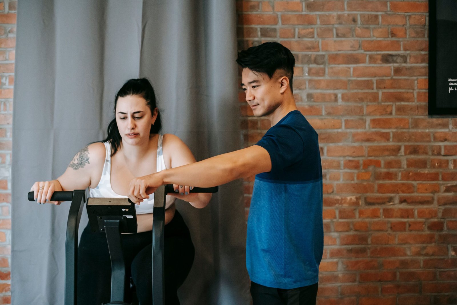 Trainer coaching a woman using a stationary exercise bike