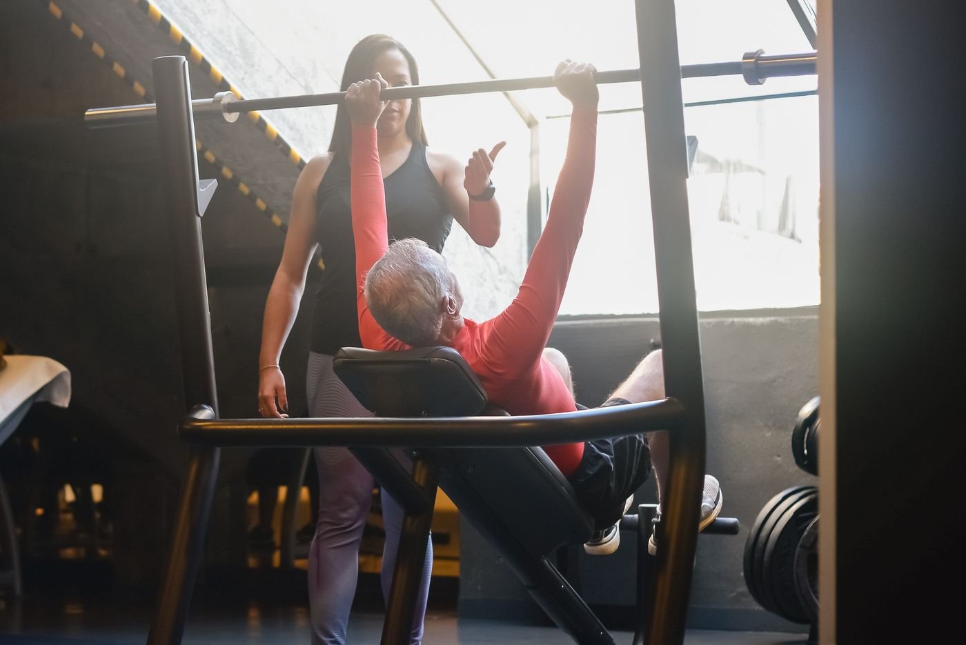 Senior man training with weights under the guidance of a coach