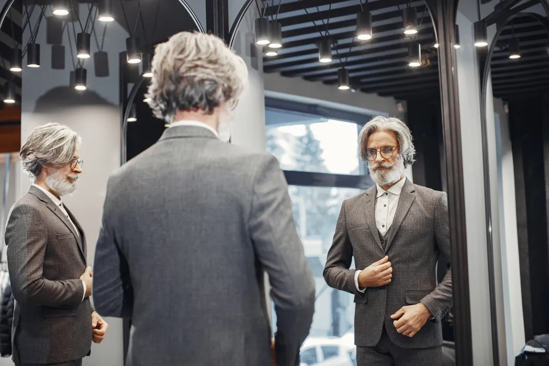 Gray-haired man examining his reflection in a mirror
