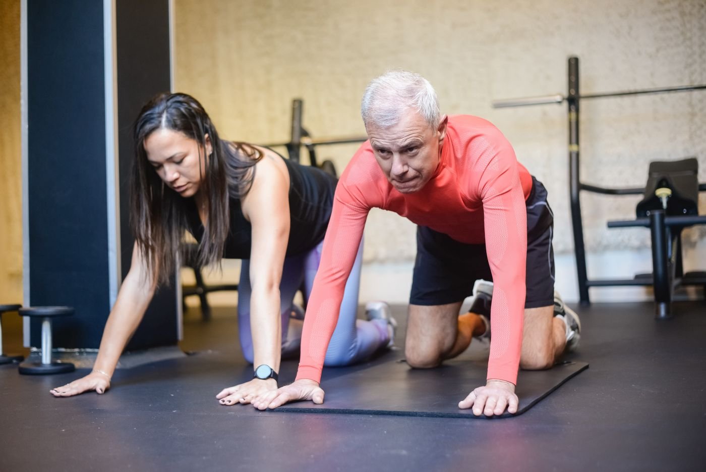 Personal trainer helping an older man exercise in a gym