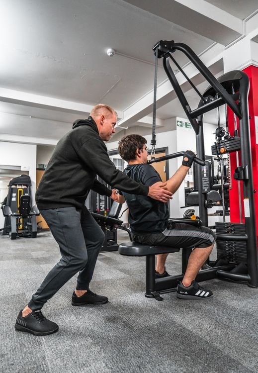 Trainer guiding a client during a gym machine exercise