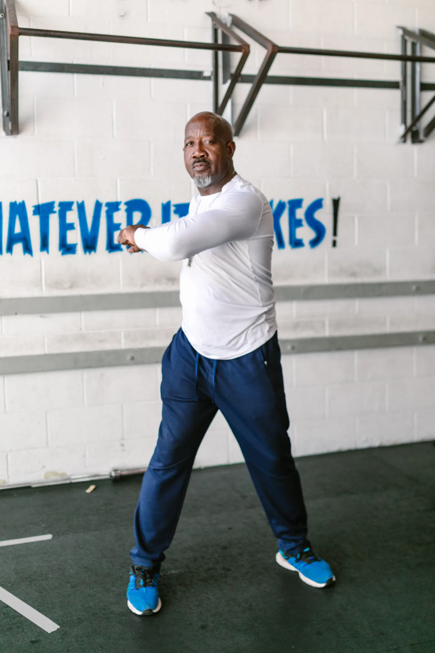 Older man warming up with a standing stretch inside a gym