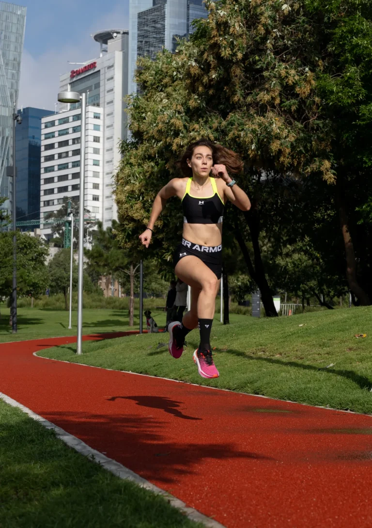 Athletic woman running on a red park track with buildings behind her