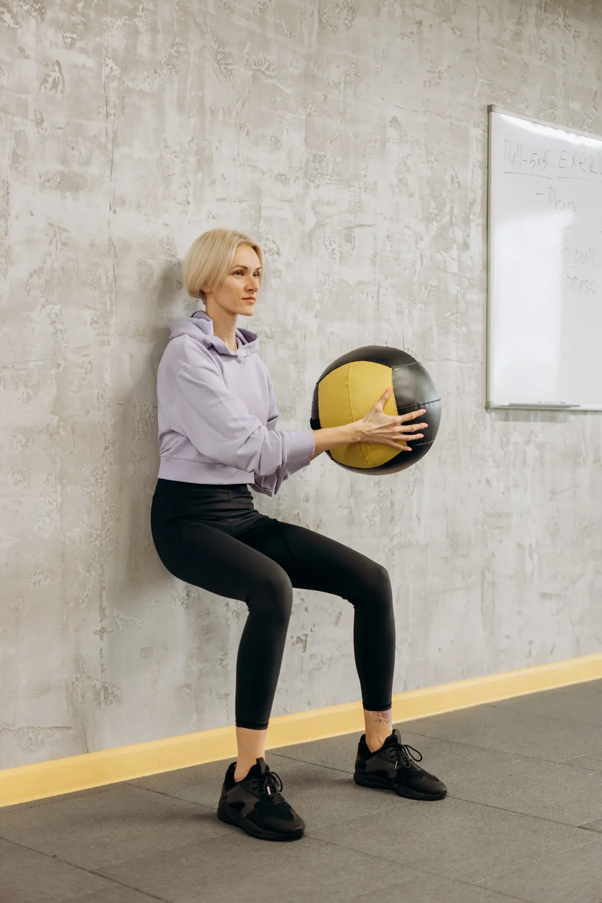 Woman maintaining a wall sit while holding a medicine ball