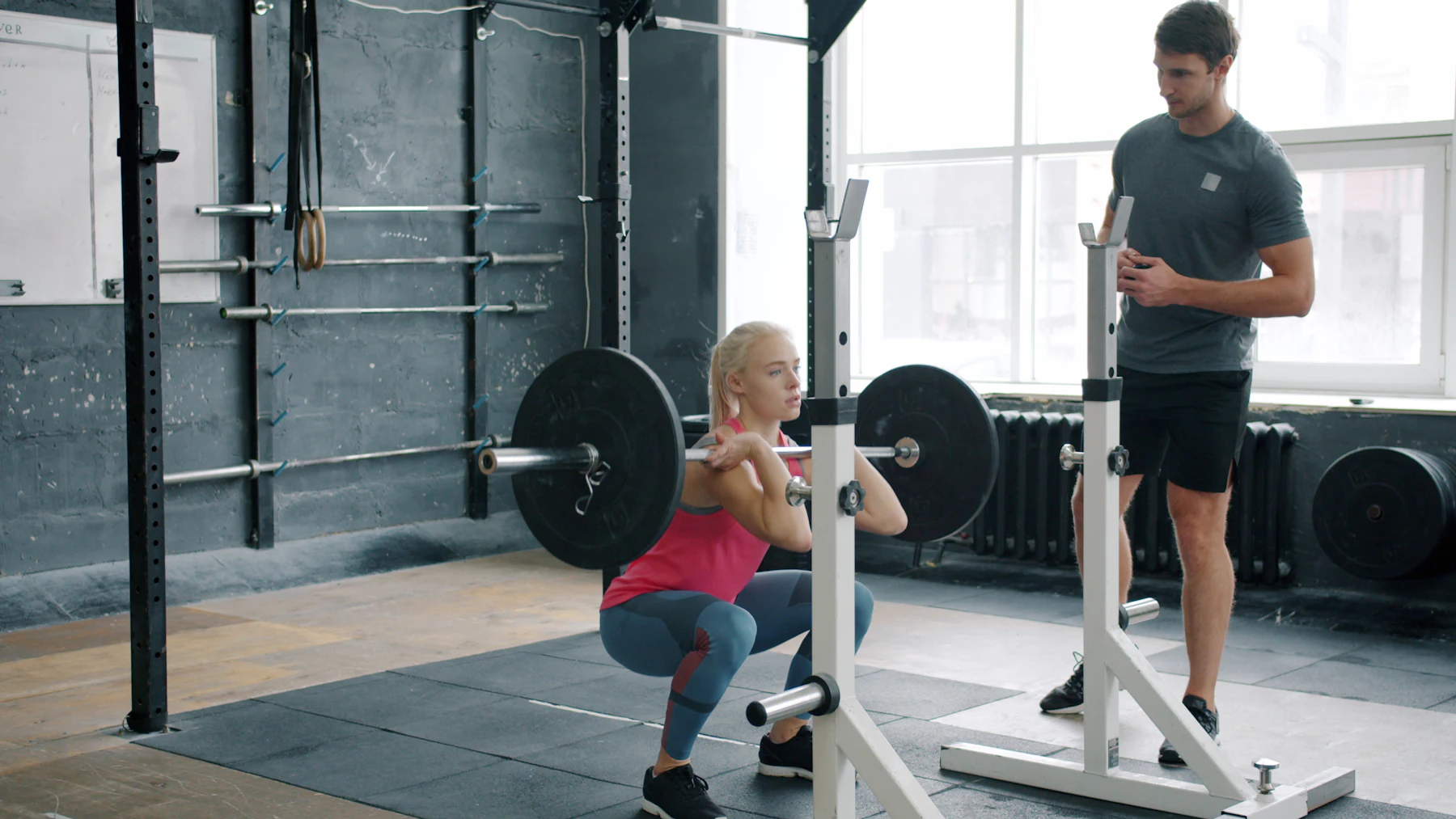 Woman performing a barbell squat while a trainer observes