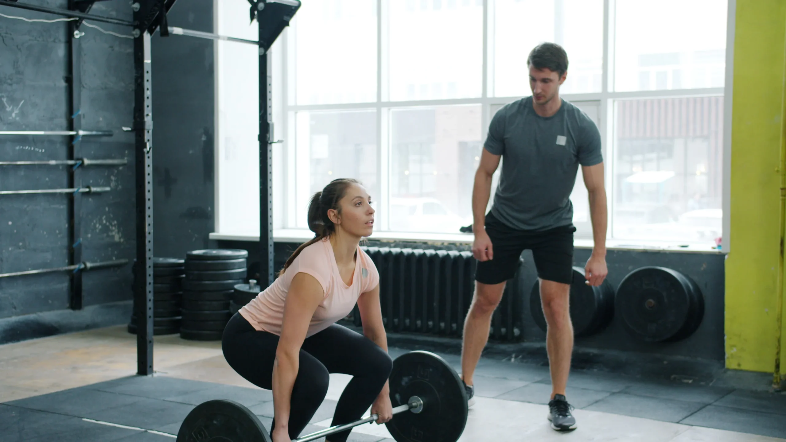 Woman lifting a barbell while a coach watches her technique