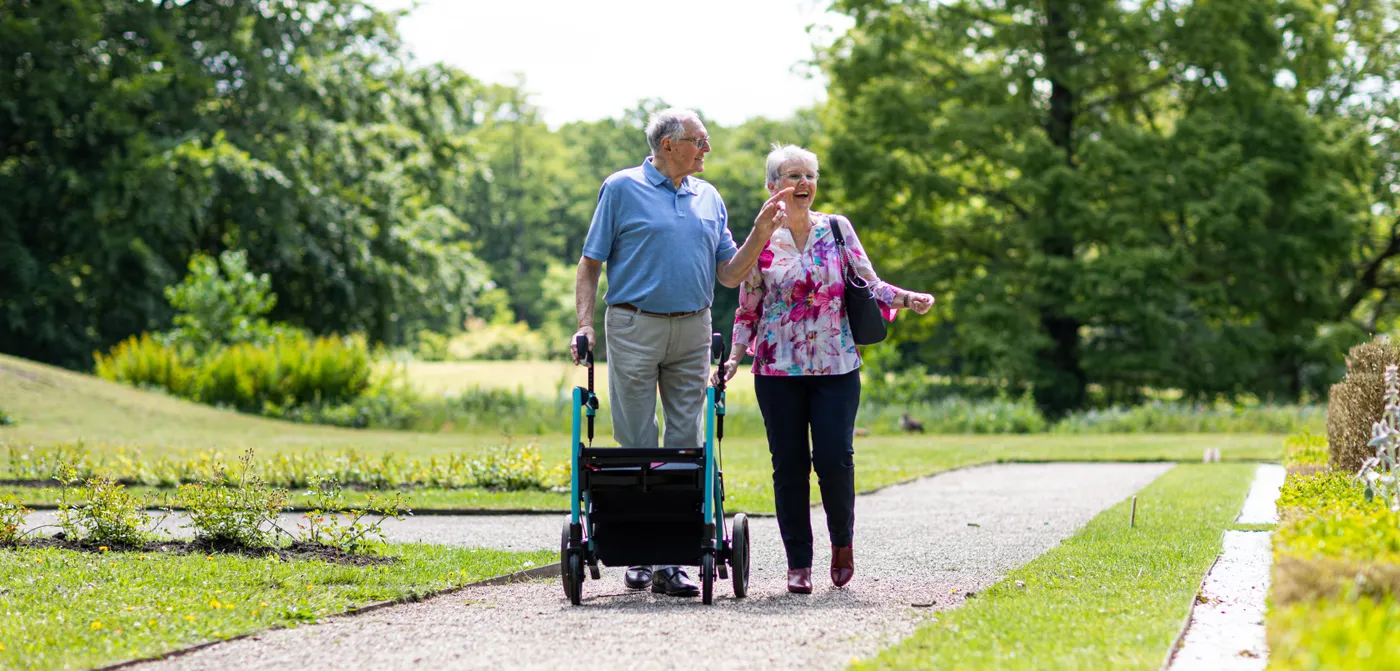 Senior couple walking with a rollator along a park path