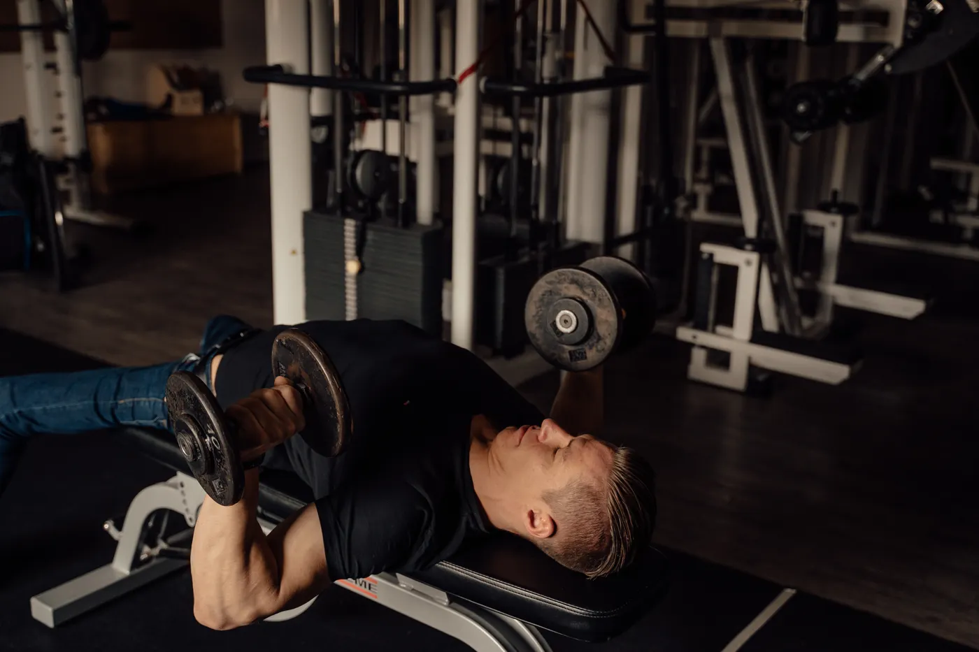 Lifter performing a dumbbell chest press on a flat gym bench