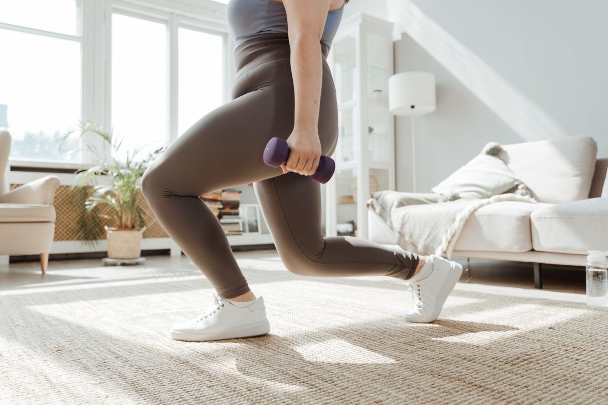 Side view of a woman performing a dumbbell lunge at home