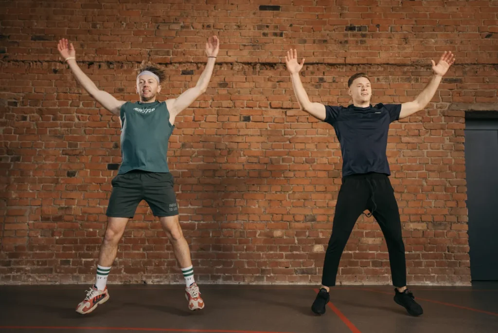 Two people doing jumping jacks in a gym