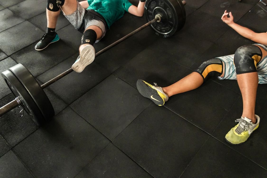 Two lifters resting on the gym floor beside loaded barbells