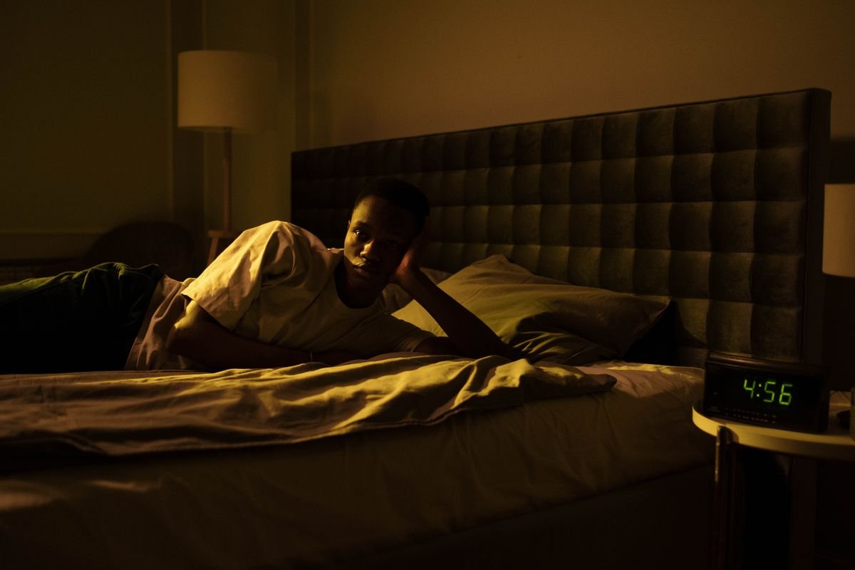 Man awake in bed early in the morning beside a clock