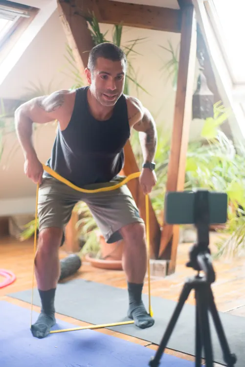 Man filming a home resistance-band workout using a phone tripod