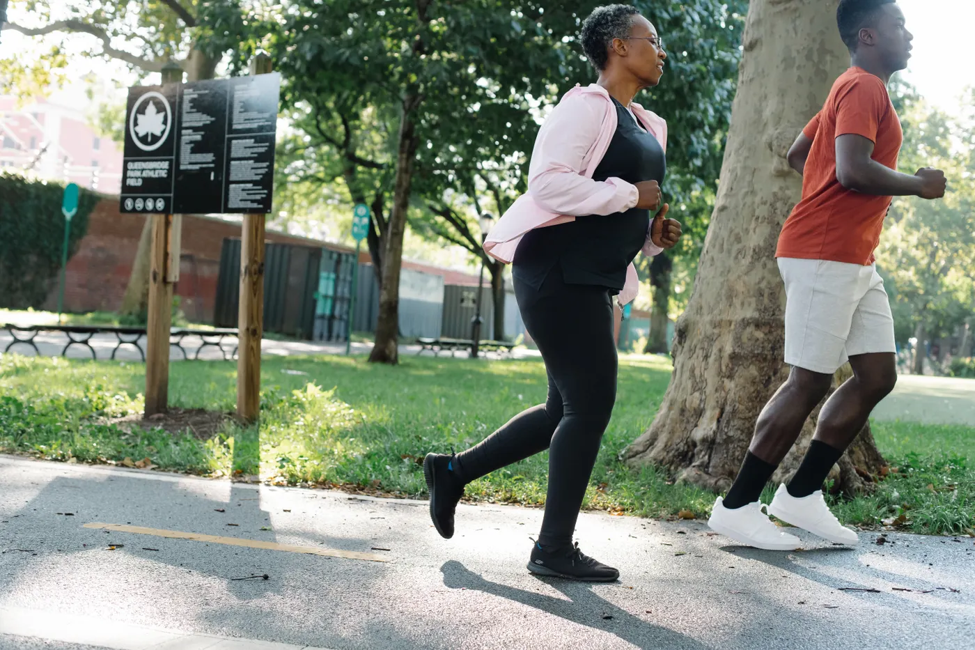 Younger man and older woman jogging together on a park trail