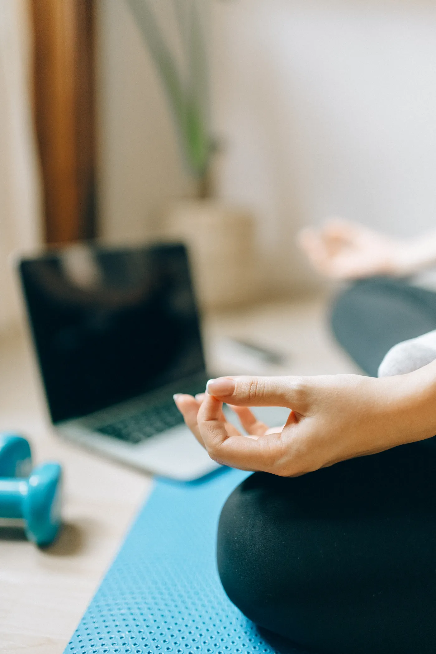 Woman resting on a mat beside dumbbells and a laptop
