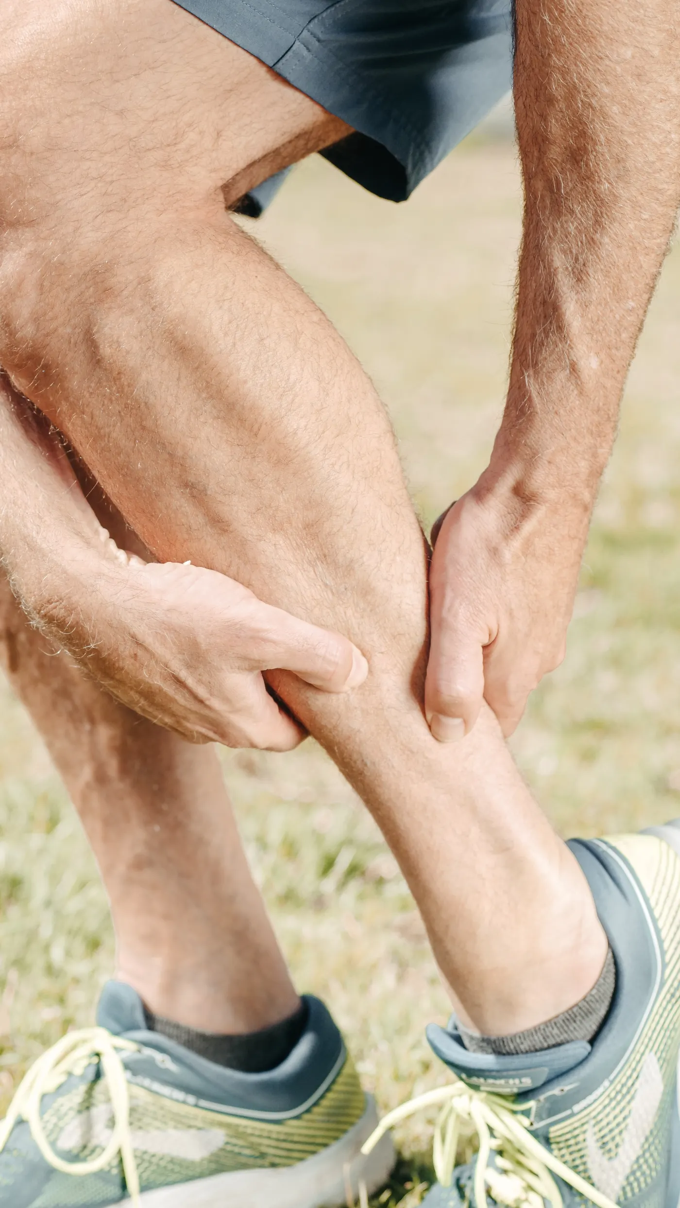 Man holding his calf while resting outdoors after physical activity