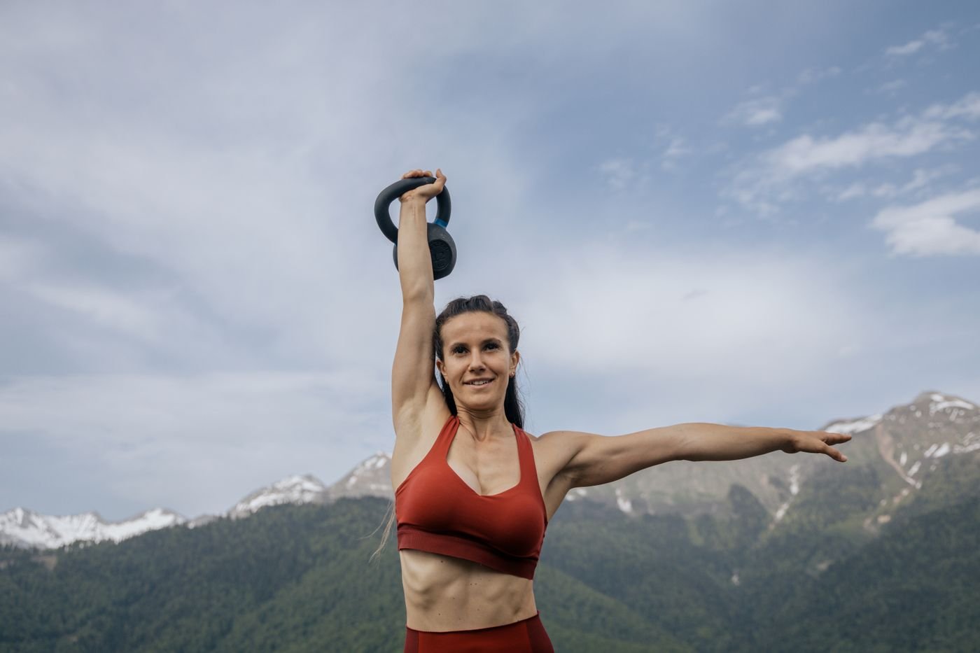 Woman lifting a kettlebell outdoors with mountains in the background