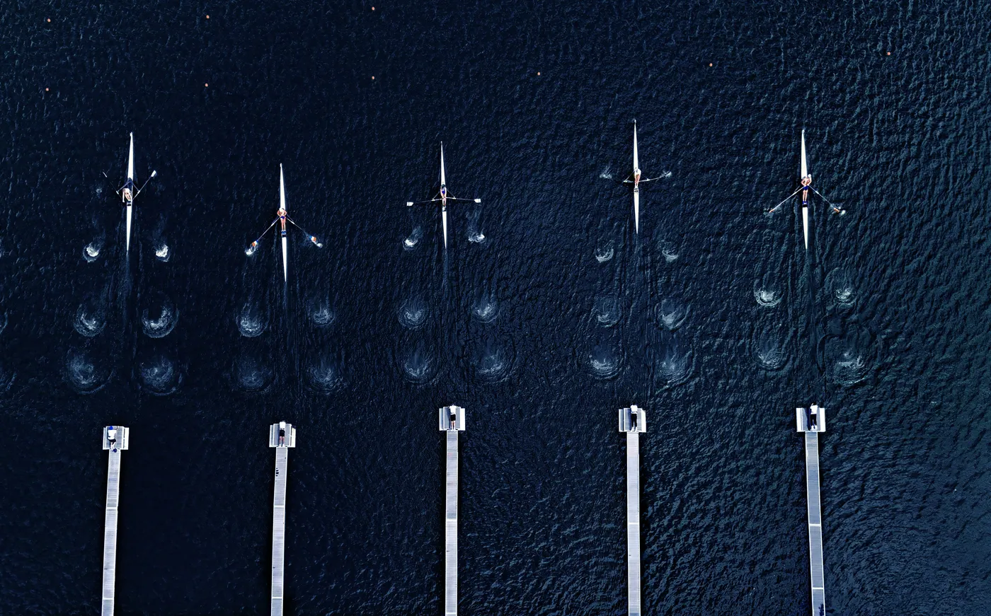 Aerial view of a rowing crew moving in sync across a calm lake