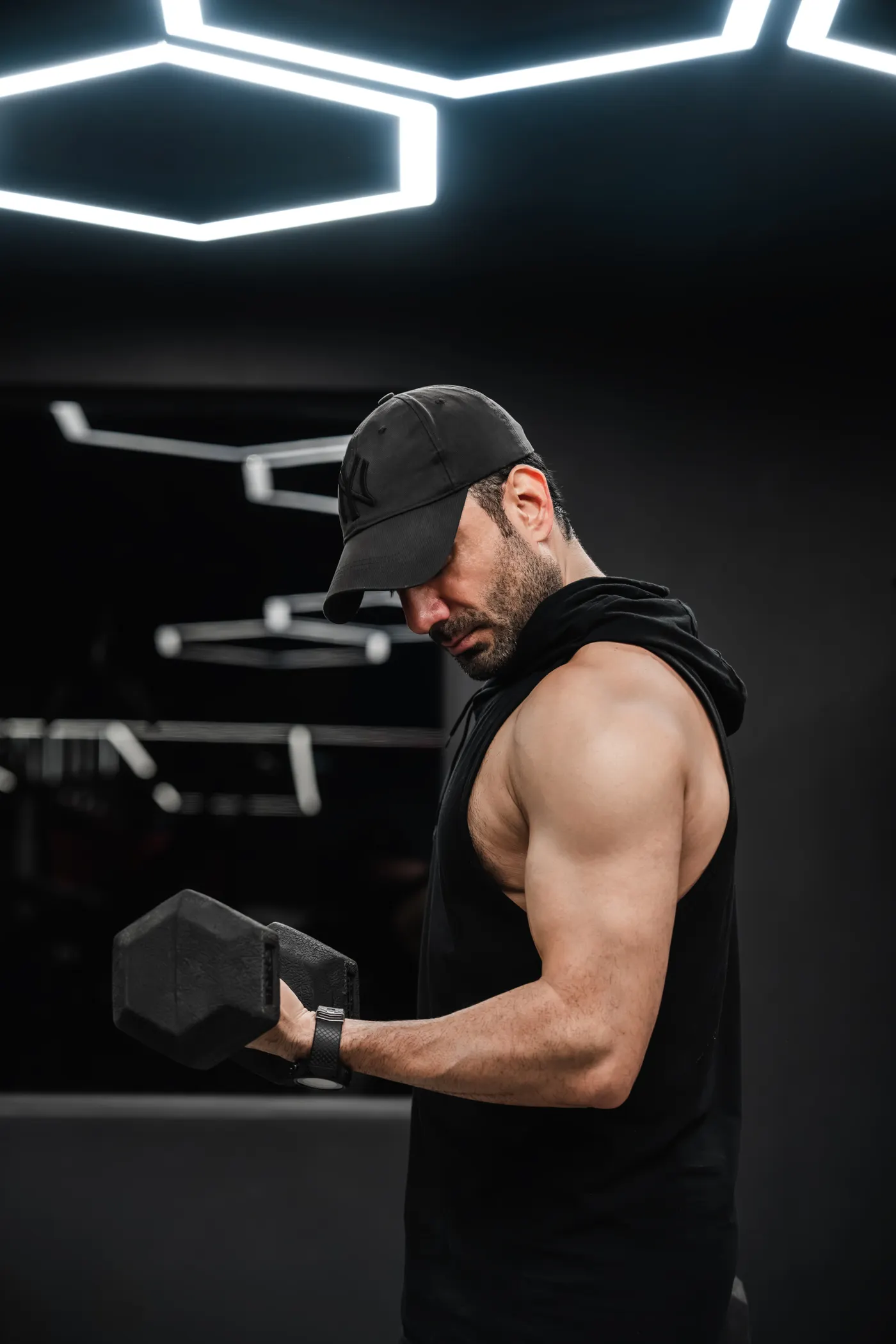 Man wearing a sleeveless hoodie lifting weights in a gym