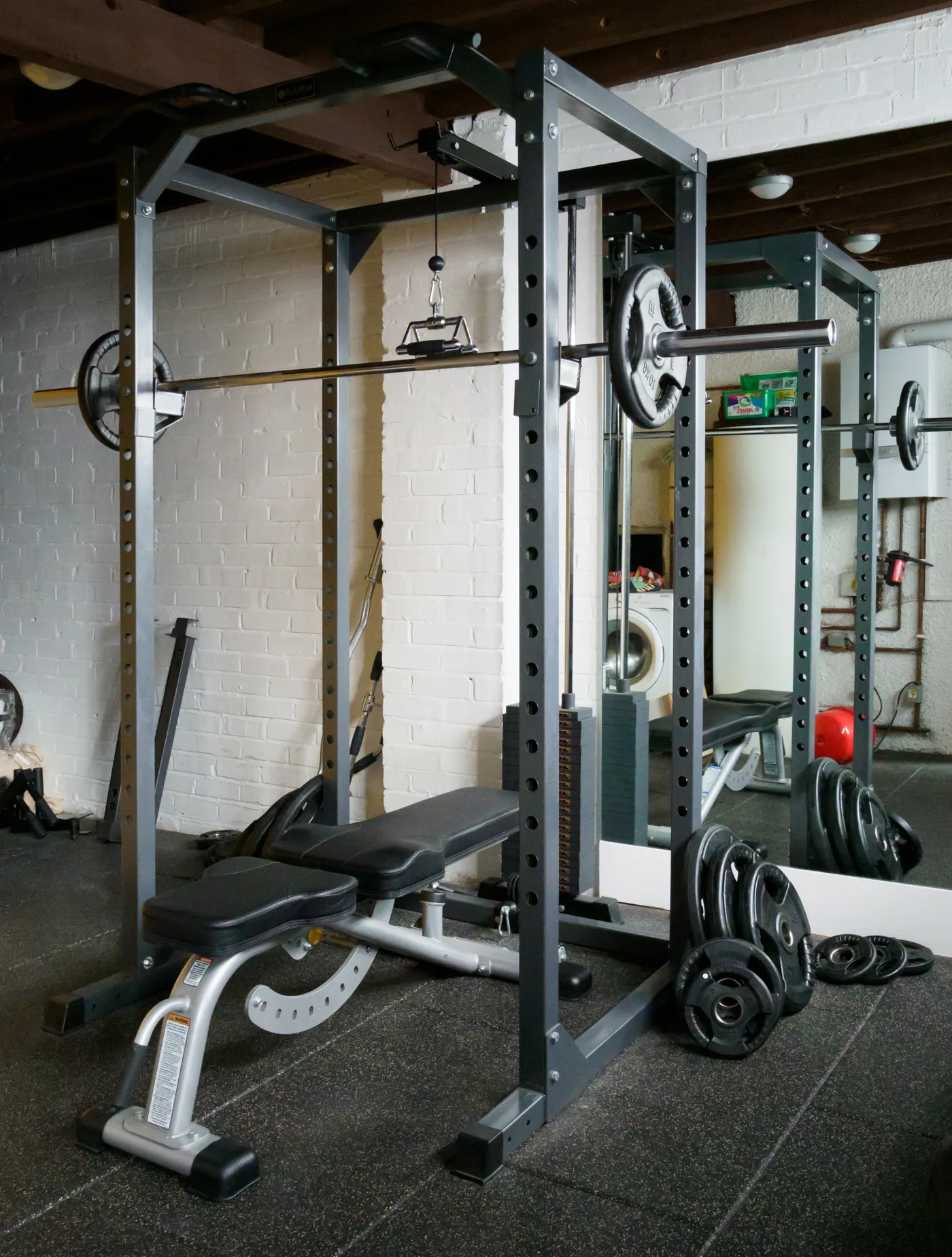 Barbell and free-weight equipment set up beside a gym mirror