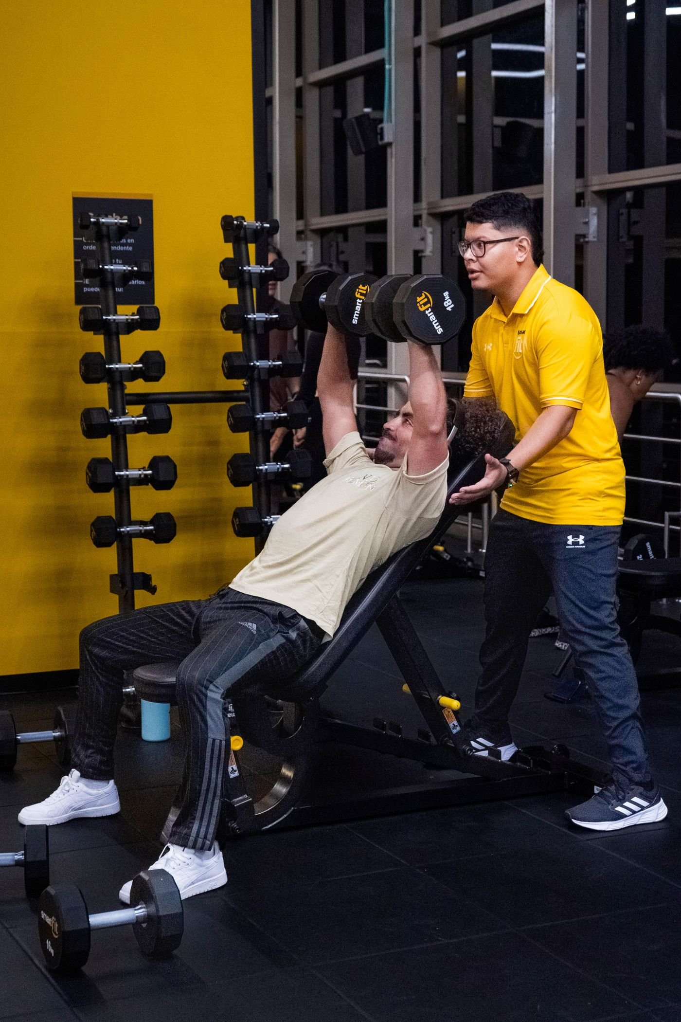 Man doing dumbbell bench presses with guidance from a trainer