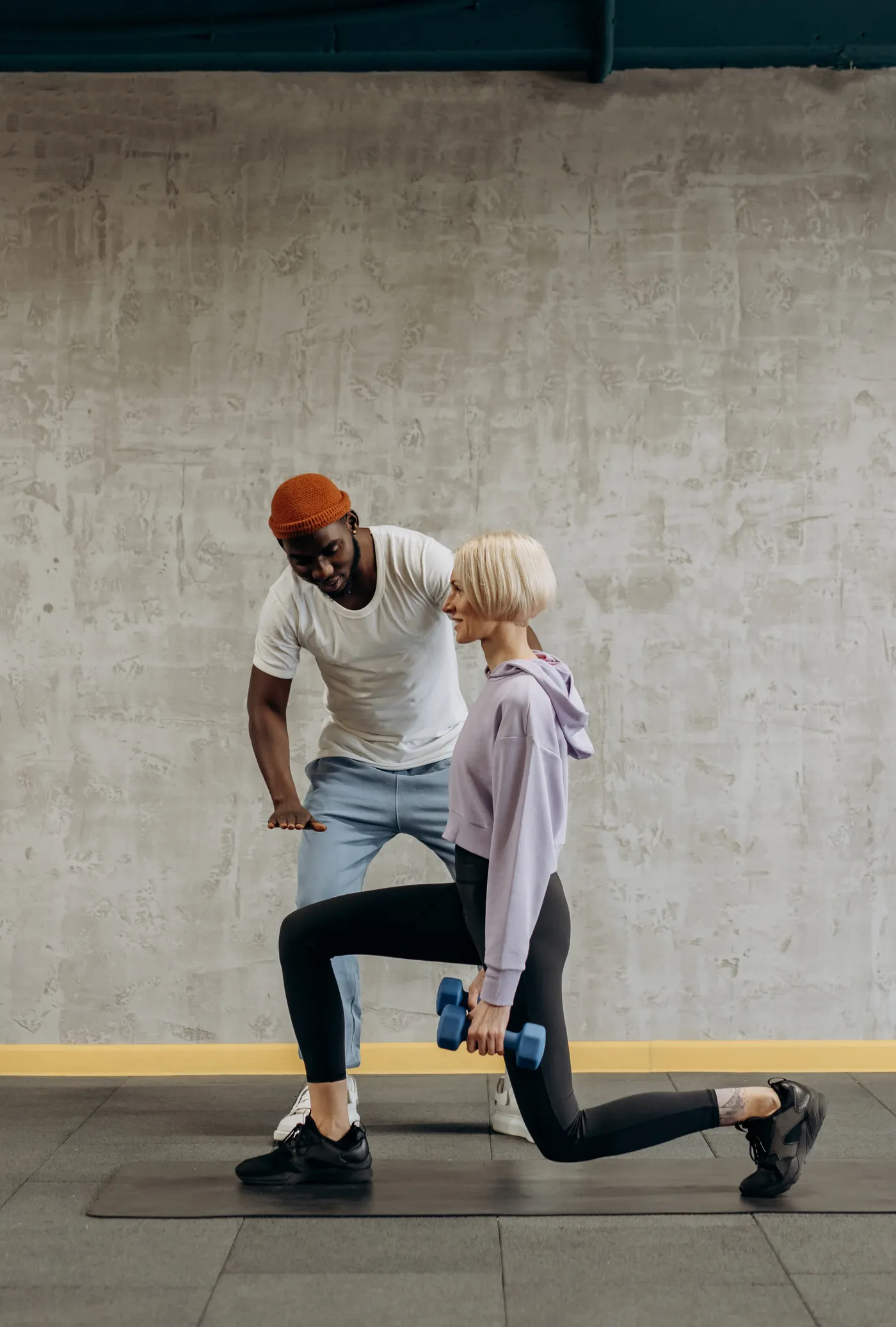 Trainer guiding a woman through a dumbbell lunge in the gym