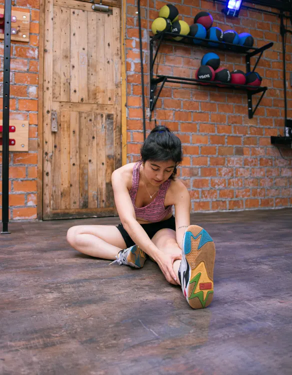 Woman holding a seated stretch in a brick-walled gym